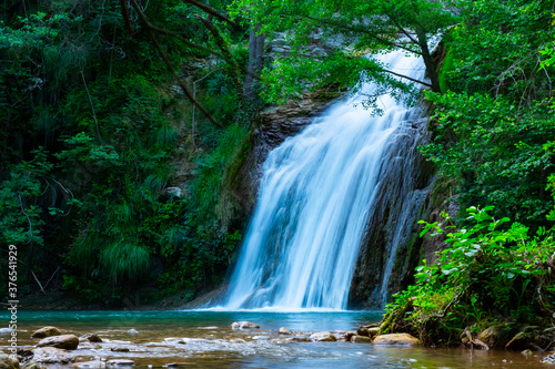 A large beautiful waterfall in a forest with blue water and a tree.