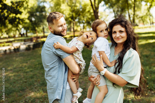 Caring parents with little kids at the park, lovely mom hold in arms joyful son, cute daughter sitting in daddy hands, family spend time together, enjoy happy moments concept © shunevich