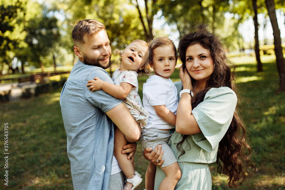 Caring parents with little kids at the park, lovely mom hold in arms joyful son, cute daughter sitting in daddy hands, family spend time together, enjoy happy moments concept