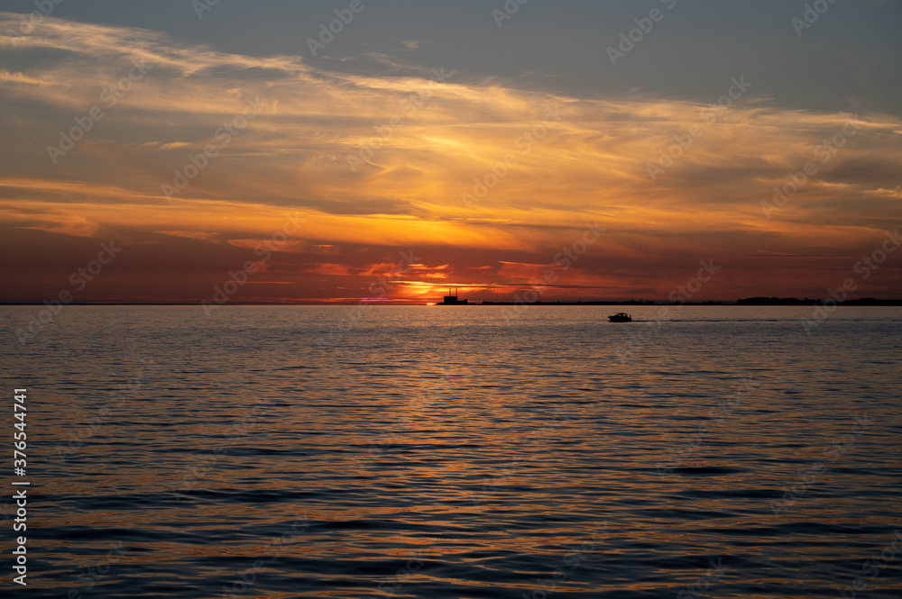 Dramatic sunset over the ocean while the silhouette of a boat and the nuclear power plant is visible on the horizon