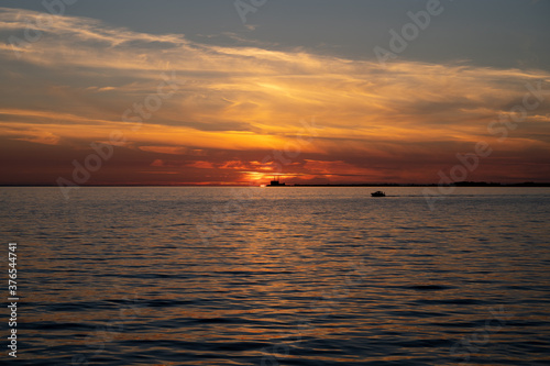 Dramatic sunset over the ocean while the silhouette of a boat and the nuclear power plant is visible on the horizon