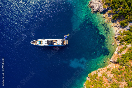 Aerial view of anchored sailing yacht in emerald sea. Aerial view of a boat. Outdoor water sports, yachting. Aerial view of anchoring yacht in open water. Ocean and sea travel and transportation © daliu