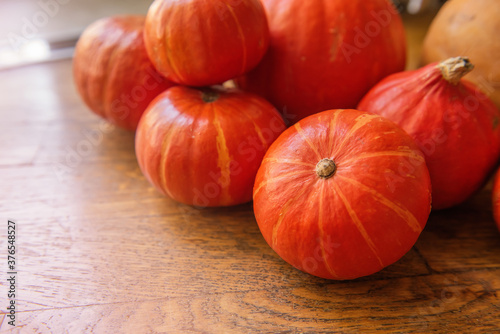 Flat lay of the small, red hokkaido pumpkins lie on the wooden floor. Halloween decorations. Copy Space. Postcard for the holiday. Autumn fresh vegetable harvest. Happy thanksgiving day. Close up 