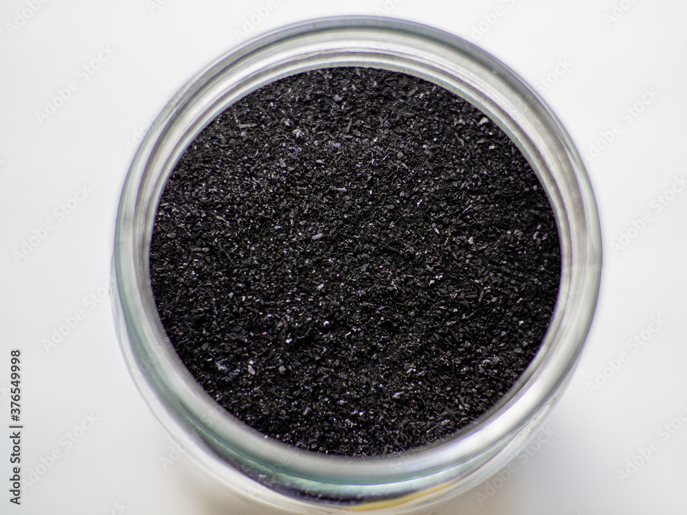 Activated charcoal powder for cosmetic face mask in a jar top view with copy space, white back