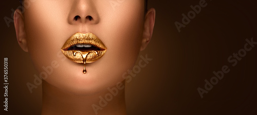 Golden lipstick closeup. Liquid metal dripping from gold lips. Beautiful makeup. Sexy lips, bright liquid paint on beautiful model girl's mouth, close-up. Lipstick. © Subbotina Anna