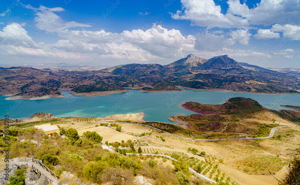 landscape of turquoise lake with mountains and hills in andalusia with road meadows and bushes