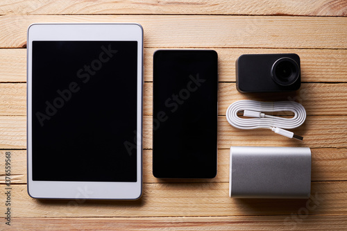 group of portable information devices on a wooden rustic desk. white tablet, silver power bank, smartphone and action video camera. blogger hardware setup