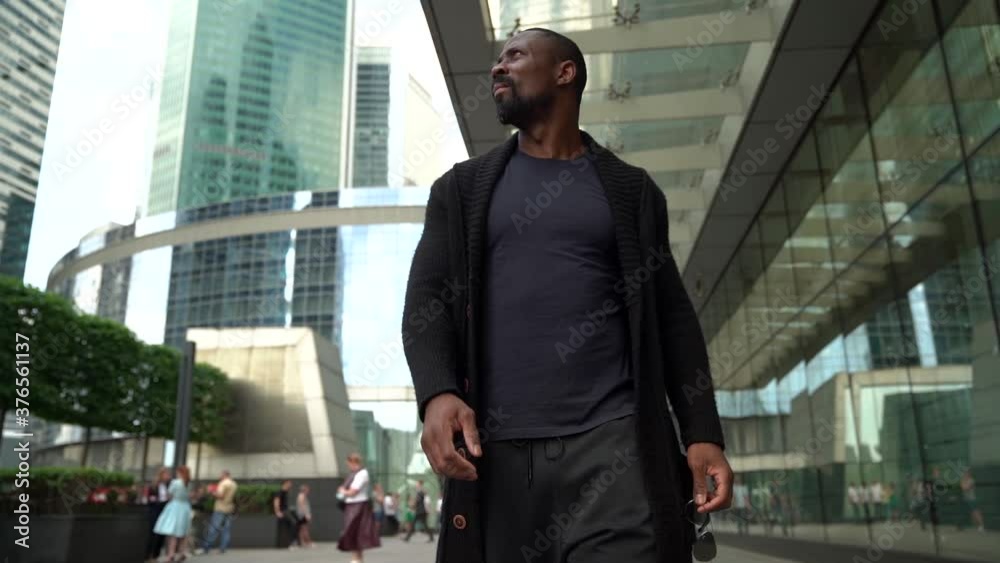 cheerful black man is walking on street at downtown of modern city, smiling and waving by hand cheerful black man is walking on street at downtown of modern city, smiling and waving by hand