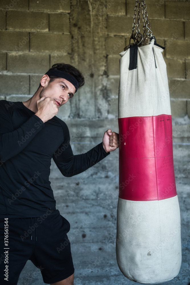 A handsome man in a black shirt punching a boxing bag