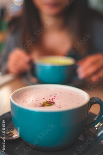 Close up on a foamy rose latte coffee with petals in a blue mug and woman in the background