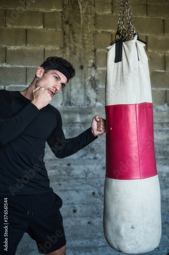 A handsome man in a black shirt punching a boxing bag © Alipasha