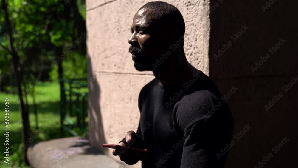 adult black man is using mobile phone at park at sunny day, typing post at social media adult black man is using mobile phone at park at sunny day, typing post at social media