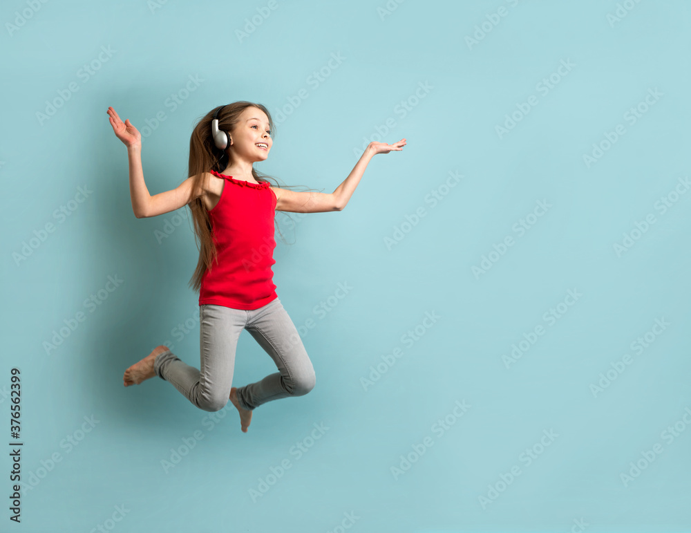 Little cheerful girl with long hair  in gray headphones listens to music, dances and has fun.