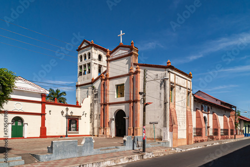 Leon, Nicaragua - November 27, 2008: San Francisco Church with bell tower is stone construction with beige and brown walls under blue sky. Tall cross on top. Street on side. Some green foliage.
