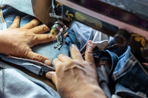 A close up hand is repairing the jeans with an old sewing machine. photo