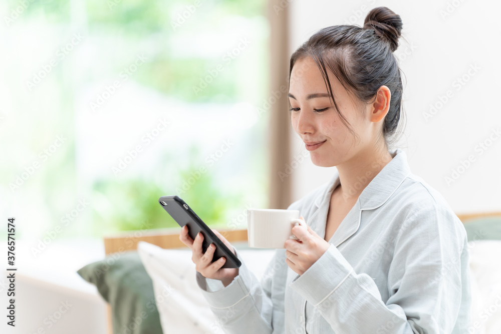 朝にスマートフォンをチェックする女性 朝にスマートフォンをチェックする女性
