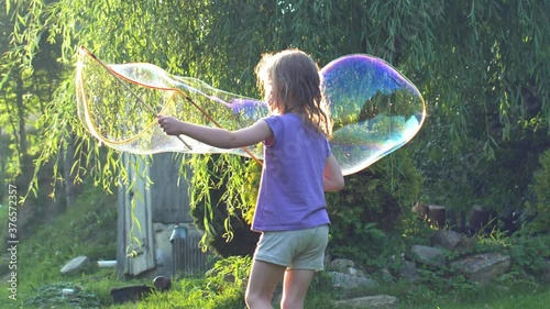 Young Girl Playing with Giant Soap Bubbles at Sunset Backlit View 