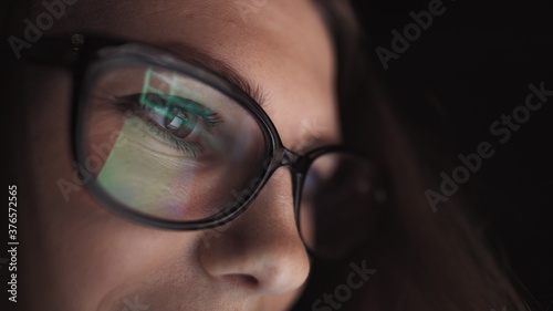 Attractive young businesswoman working at night via computer at office with, closeup of hipster student girl browsing the internet, looking at monitor of modern computer, focus on the glasses