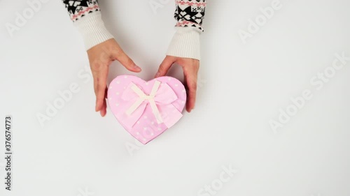 baked round multi-colored macarons in a heart-shaped pink cardboard box, female hands take dessert, top view