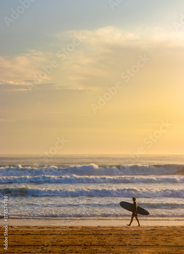 Surfer walking along beach with surfboard on Many Beach, Australia. 