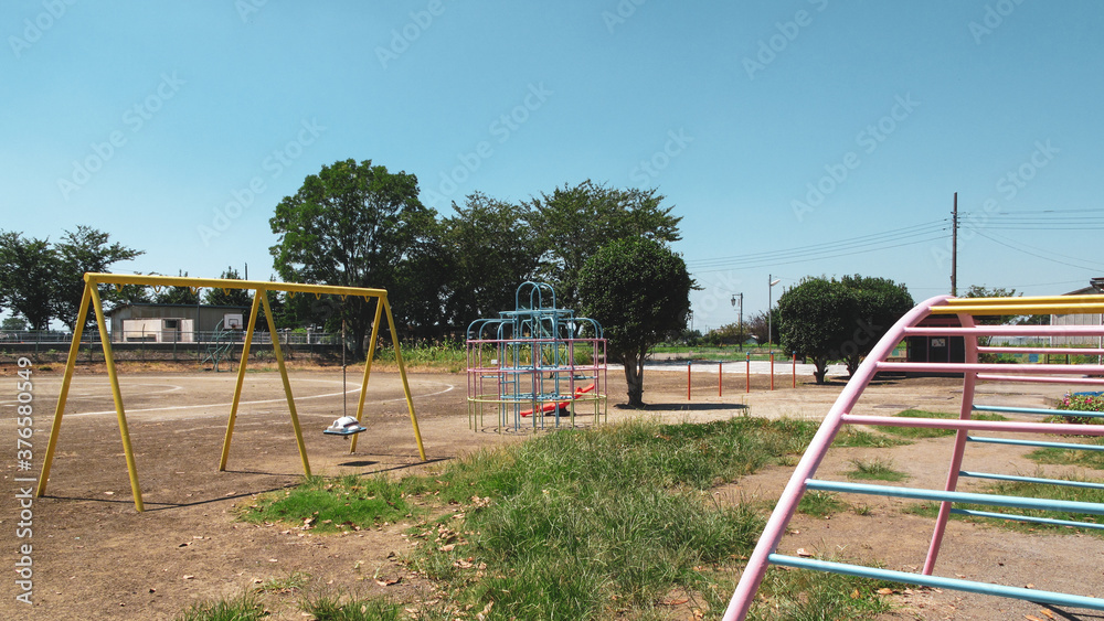 A traditional elementary school playground with play equipment, weeds, and a blue sky in rural Japan on a sunny day.