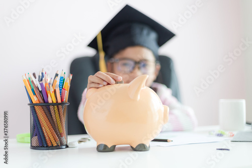 Little Asian girl putting the coin into piggy bank and smile with happiness for money saving to wealthness in the future of education concept select focus shallow depth of field photo