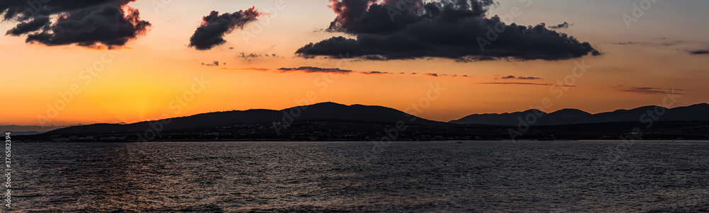 Panorama of a colorful sea sunset, which smoothly goes behind the mountains of the city of Gelendzhik. Cloudy and dark summer landscape. The city was temporarily left without electricity