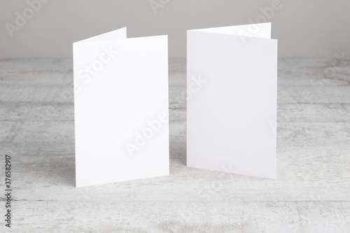 Two white greeting cards mockup, standing upright on a white wooden desk. Blank closed cards template. 