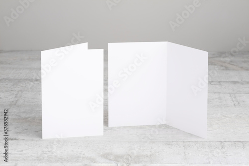 Two white greeting cards mockup, standing upright on a white wooden desk. Blank, open and closed cards template. 