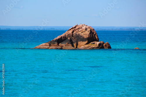 Scenic ancient Sugar Loaf Rock South Western Australia in the blue Indian Ocean is a popular fishing and hiking destination with its treeless green dunes and  splashing waves on old eroded rocks. © allymoon