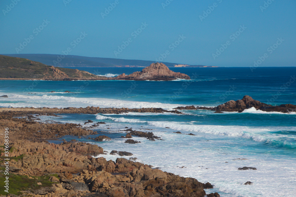 Scenic ancient Sugar Loaf Rock South Western Australia in the blue Indian Ocean is a popular fishing and hiking destination with its treeless green dunes and  splashing waves on old eroded rocks.