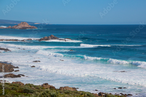 Scenic ancient Sugar Loaf Rock South Western Australia in the blue Indian Ocean is a popular fishing and hiking destination with its treeless green dunes and splashing waves on old eroded rocks.
