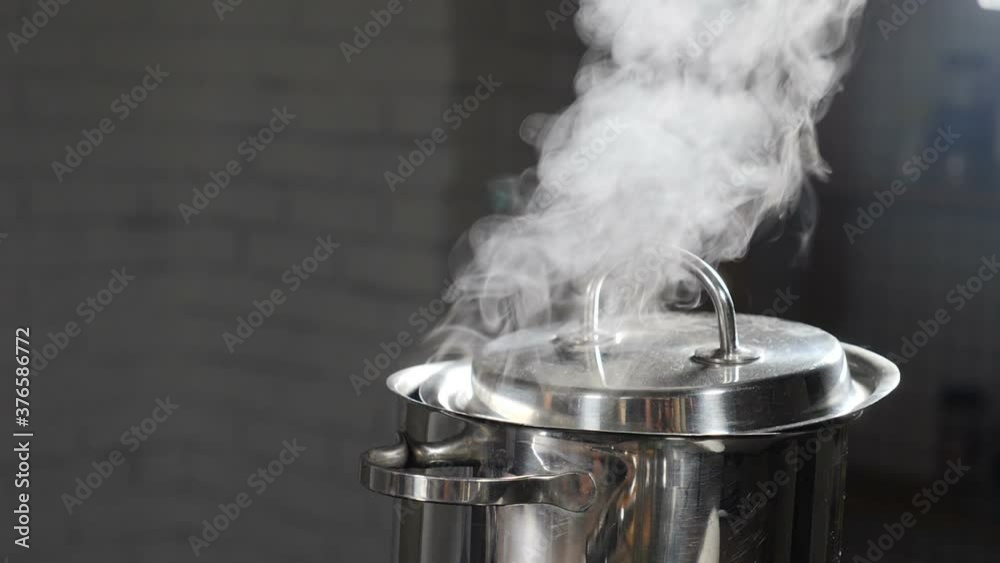 Steam or Vapour clouds rising from boiling water in saucepan on stove. Steam from pan while cooking. Cooking process in slow motion. Steam and white smoke rising on dark background. Full hd