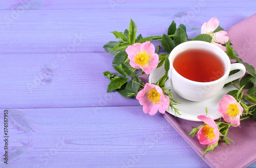 Cup of tea and wild rose flower on purple boards, copy space for text