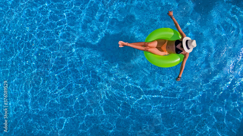 Beautiful woman in hat in swimming pool aerial view from above, young girl in bikini relaxes and swims on inflatable ring donut and has fun in water on vacation 