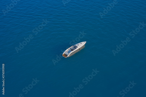 Drone view of a boat. Lonely boat mooring on the water. Aerial view of a yacht on blue water. Top view of a white boat in the blue sea. luxury motor boat. © Berg