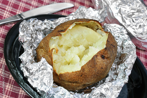 One open baked potato on aluminum foil, unwrapped.