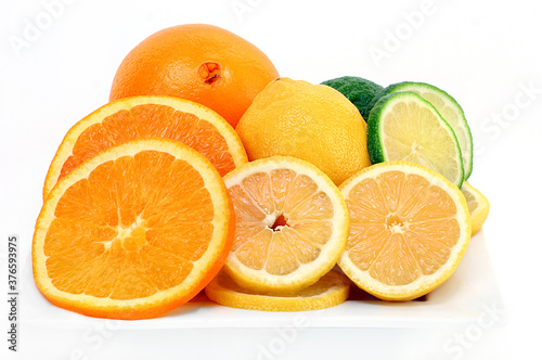 Citrus fruits of oranges, lemons and limes cut and whole on a white plate and background.