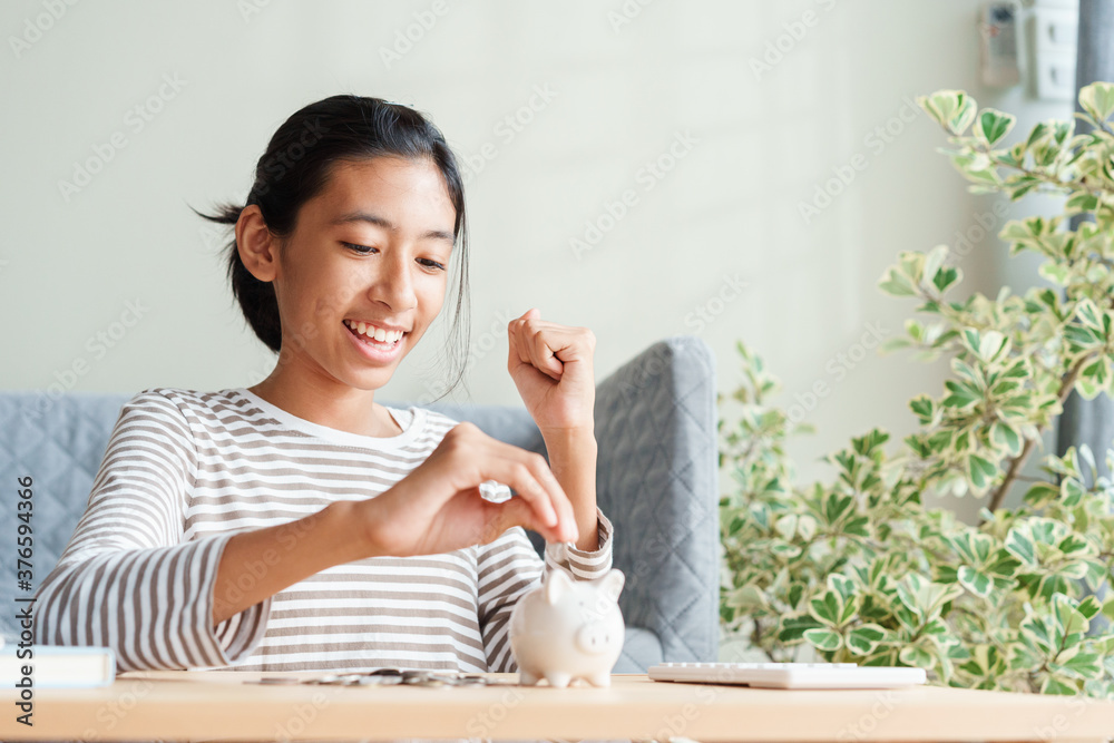 Success Asian young girl is putting coins in a piggy bank at home, finance and saving money for future concept Success Asian young girl is putting coins in a piggy bank at home, finance and saving money for future concept