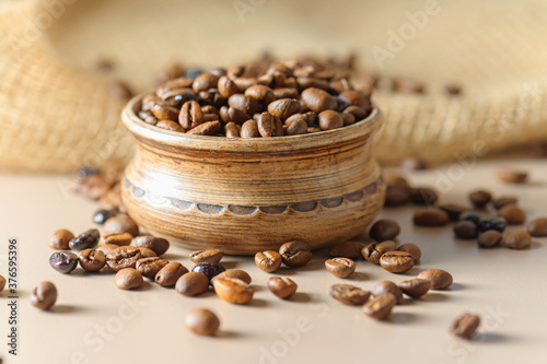 A pot of coffee beans on a sacking. Roasted coffee beans are scattered on the table. A mix of different types of coffee roasting.