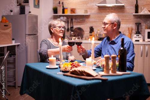 Cheerful old couple celebrating marriage with wine and festive dinner. Happy senior elderly couple dining together in the cozy kitchen  enjoying the meal  celebrating their anniversary.