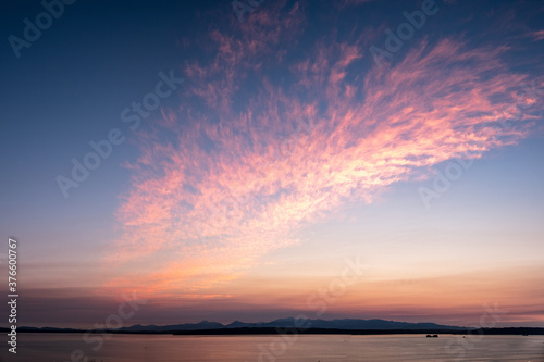 The clouds reflect the colorful sunset over Puget Sound as the sun slowly sets behind the mountains