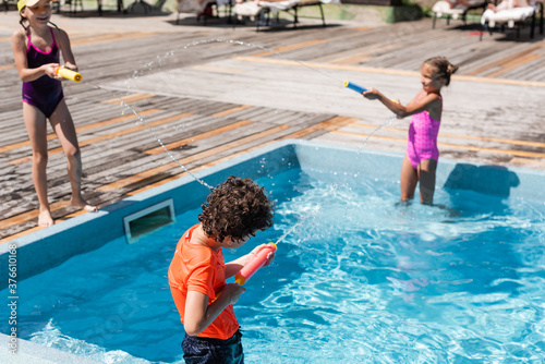 selective focus of boy and two girls fighting with water guns near pool