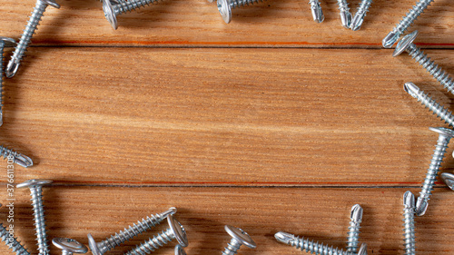 Self-cutters on a wood brown background banner with space for text. Construction tools, self-tapping screws for fastening. Black screw hardware.