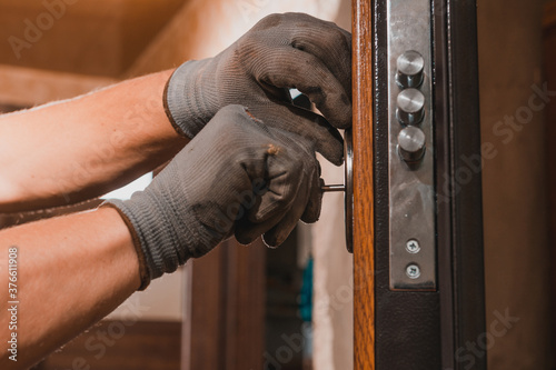 Close-up, the carpenter installs a custom lock in the front metal door, using a drill and hammer and other tools. photo