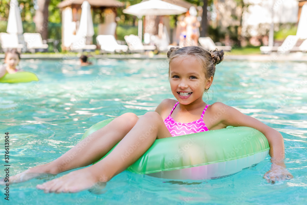 child looking at camera while floating in pool on inflatable ring