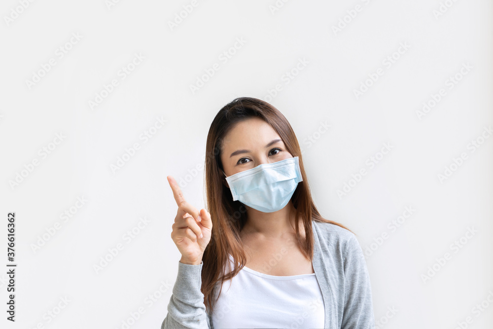 Closeup portrait of beautiful young Asian woman with ptrotective face mask pointing with index finger upwards, isolated on white background. Positive thinking concept. Copy space Closeup portrait of beautiful young Asian woman with ptrotective face mask pointing with index finger upwards, isolated on white background. Positive thinking concept. Copy space