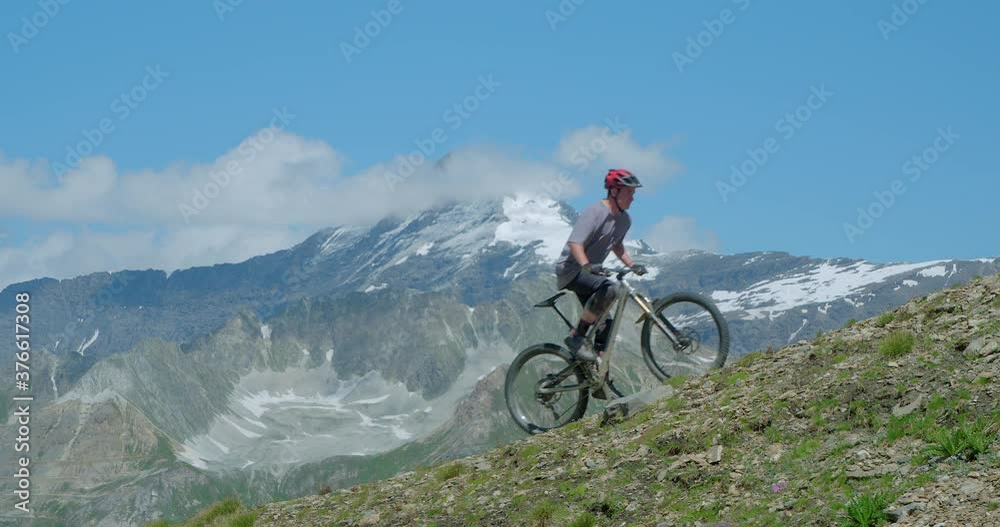 Two mountain bikers peddling hard up a steep high altitude mountainside with glaciers in background. Peddling up steep mountains at 12,000ft above sea level is extremely demanding on the human body. Two mountain bikers peddling hard up a steep high altitude mountainside with glaciers in background. Peddling up steep mountains at 12,000ft above sea level is extremely demanding on the human body.