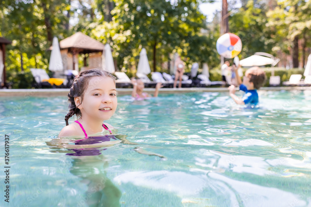 joyful girl looking at camera while spending time in swimming pool