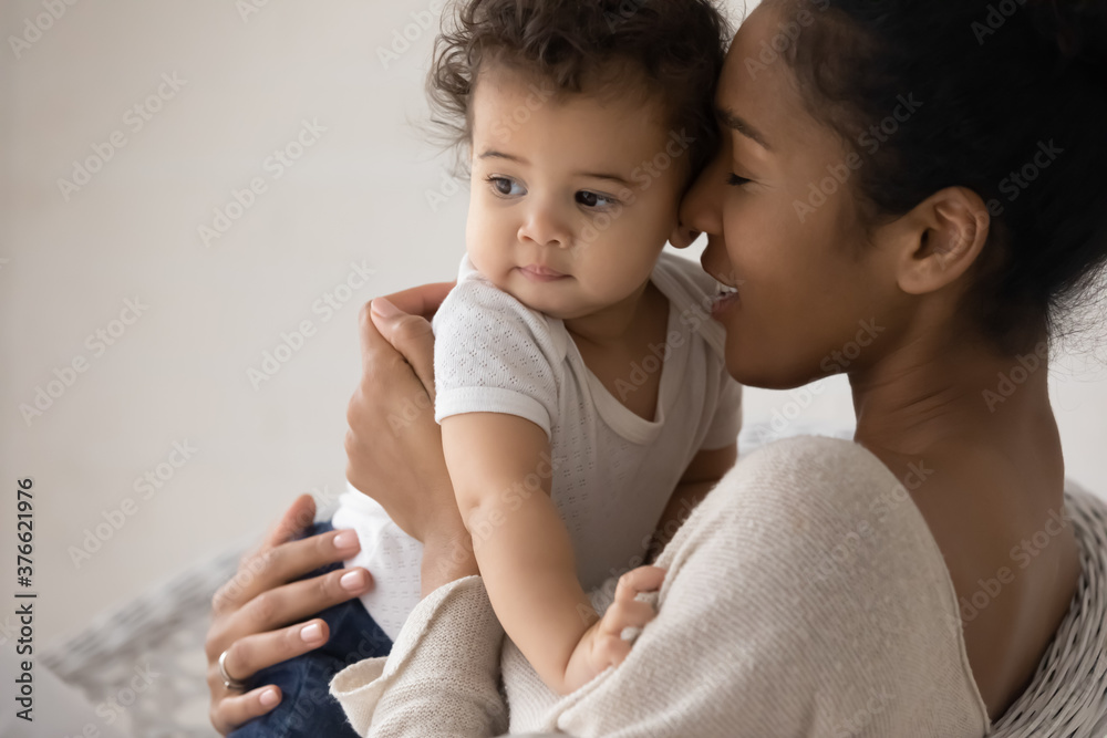 Head shot caring young mixed race mother cuddling little biracial funny baby toddler daughter or son, enjoying sweet family closeness moment indoors, showing love and devotion, childcare concept. Head shot caring young mixed race mother cuddling little biracial funny baby toddler daughter or son, enjoying sweet family closeness moment indoors, showing love and devotion, childcare concept.